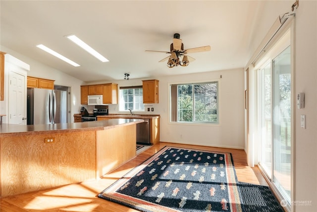 kitchen featuring kitchen peninsula, ceiling fan, stainless steel appliances, vaulted ceiling with skylight, and light hardwood / wood-style floors