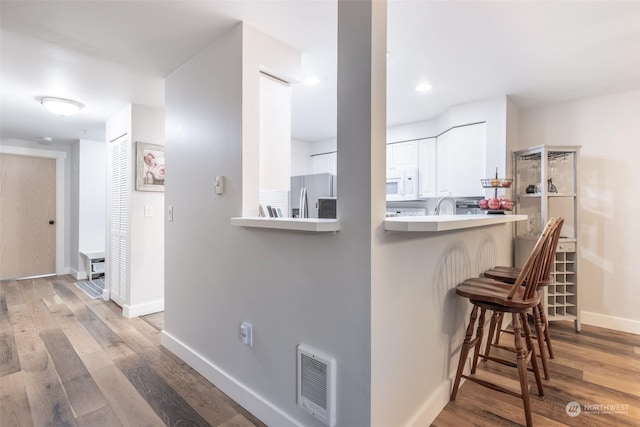 kitchen with a breakfast bar, white cabinetry, kitchen peninsula, stainless steel refrigerator with ice dispenser, and light wood-type flooring