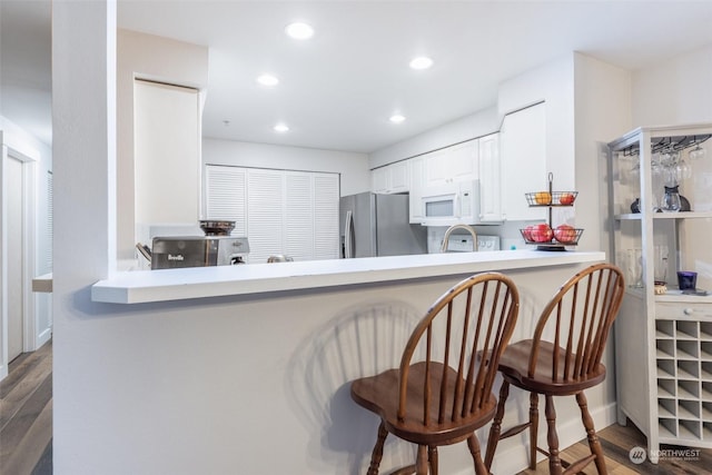 kitchen featuring a breakfast bar, dark hardwood / wood-style flooring, stainless steel fridge, kitchen peninsula, and white cabinets