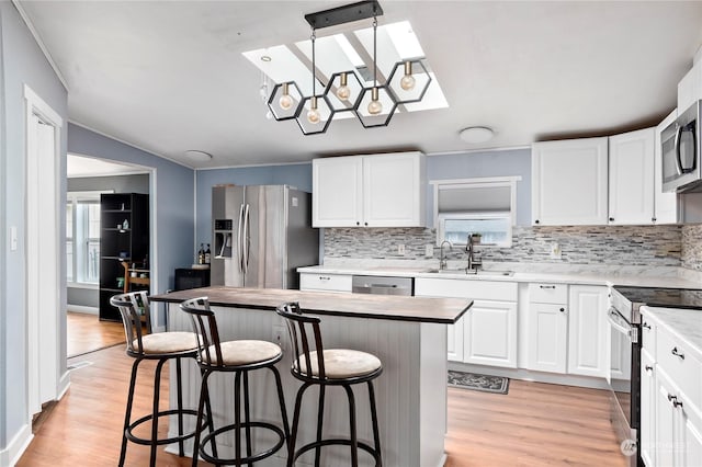 kitchen featuring a kitchen island, appliances with stainless steel finishes, white cabinetry, sink, and hanging light fixtures