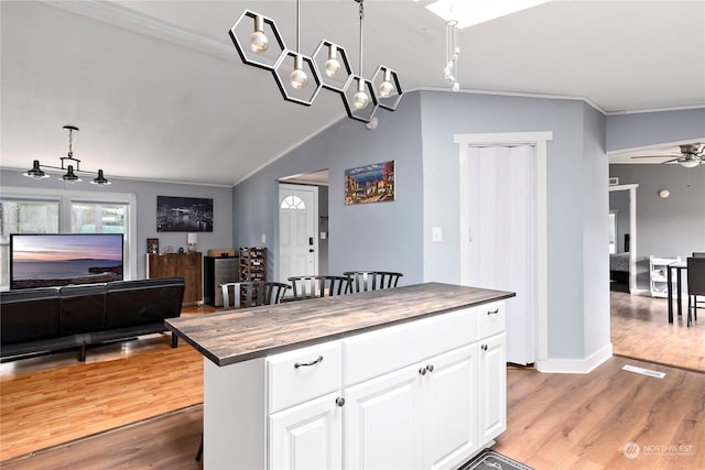 kitchen featuring a kitchen island, butcher block countertops, decorative light fixtures, white cabinetry, and light hardwood / wood-style floors