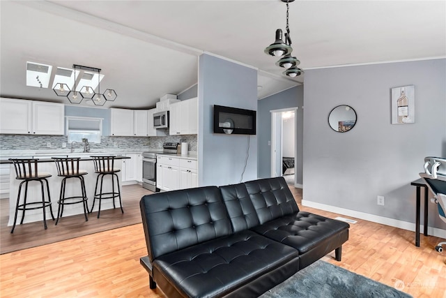 living room with lofted ceiling, sink, crown molding, and light hardwood / wood-style flooring