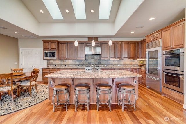 kitchen with light stone counters, appliances with stainless steel finishes, hanging light fixtures, and a center island with sink