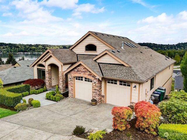 view of front of house featuring a garage, a shingled roof, concrete driveway, stone siding, and a water view