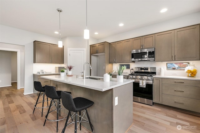 kitchen featuring sink, appliances with stainless steel finishes, hanging light fixtures, a center island with sink, and light wood-type flooring