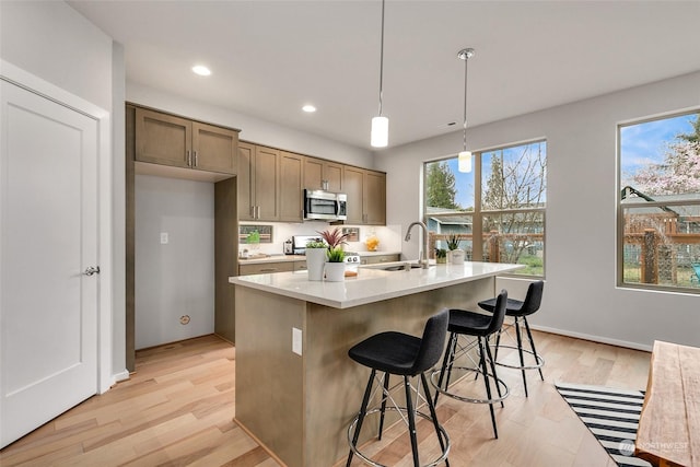 kitchen with pendant lighting, a wealth of natural light, an island with sink, and light wood-type flooring