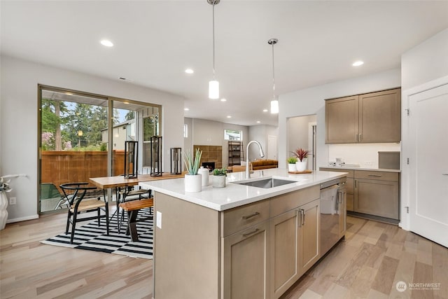 kitchen with pendant lighting, dishwasher, sink, light hardwood / wood-style floors, and a center island with sink