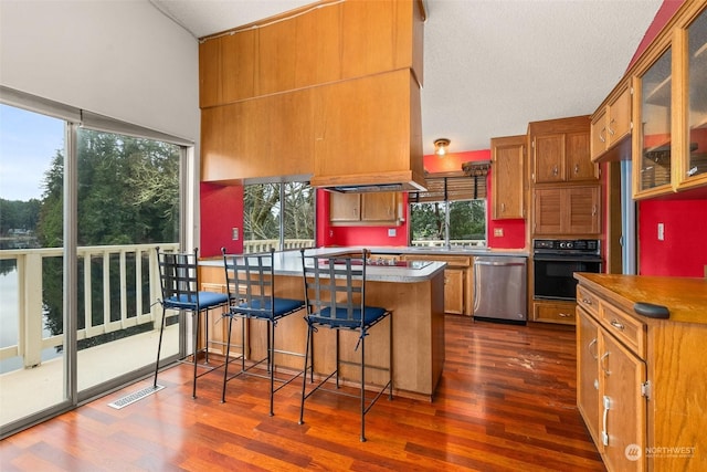 kitchen with dark wood-type flooring, stainless steel dishwasher, a breakfast bar, and oven