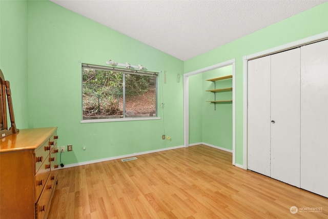 unfurnished bedroom featuring vaulted ceiling, a textured ceiling, and light hardwood / wood-style flooring