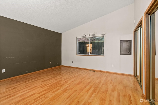 spare room with lofted ceiling, a textured ceiling, and light wood-type flooring