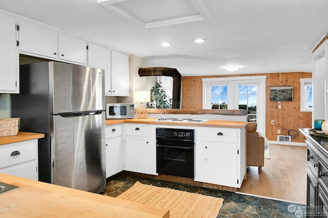 kitchen featuring appliances with stainless steel finishes, butcher block counters, white cabinets, kitchen peninsula, and wood walls