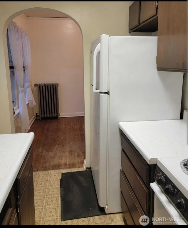 kitchen featuring stove, radiator heating unit, light hardwood / wood-style floors, white refrigerator, and dark brown cabinetry