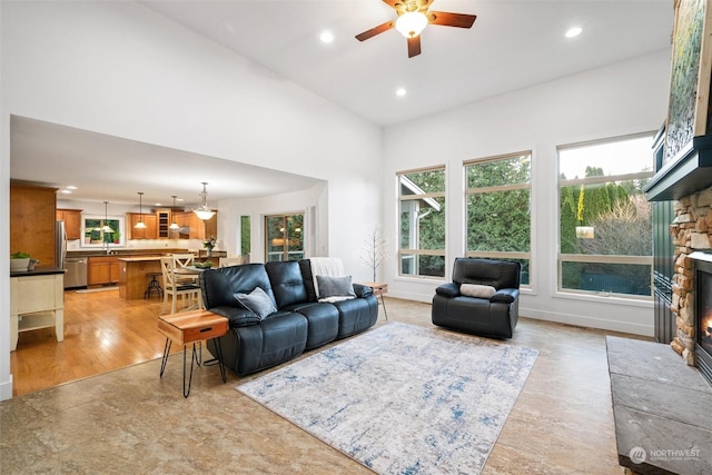 living room featuring ceiling fan, a towering ceiling, and a fireplace