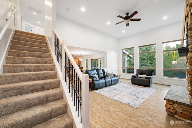 living room with a high ceiling, ceiling fan, and light wood-type flooring