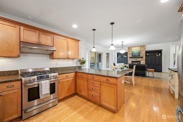 kitchen with light hardwood / wood-style flooring, stainless steel gas range, a stone fireplace, decorative light fixtures, and kitchen peninsula