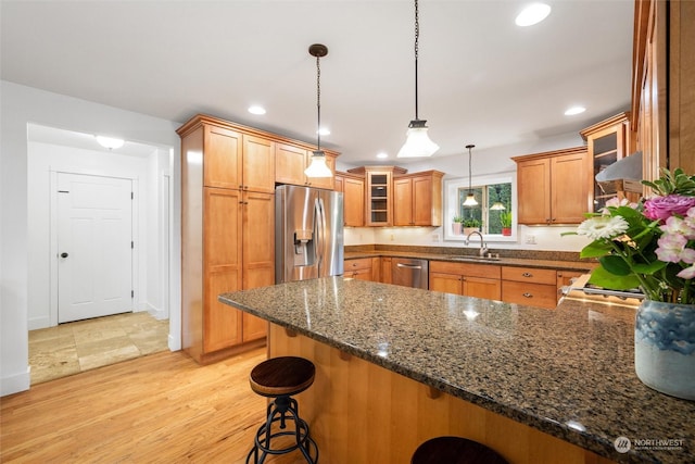 kitchen featuring a breakfast bar area, light wood-type flooring, appliances with stainless steel finishes, pendant lighting, and dark stone counters