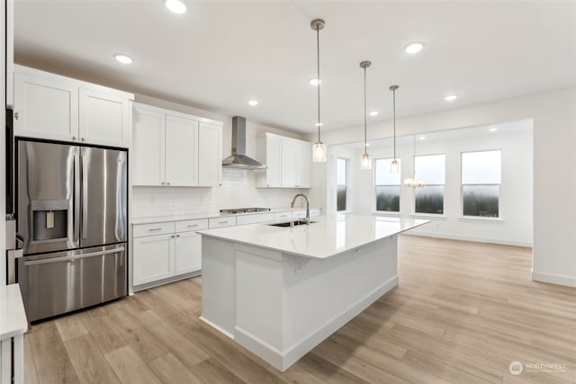 kitchen featuring wall chimney exhaust hood, sink, white cabinetry, hanging light fixtures, and stainless steel appliances