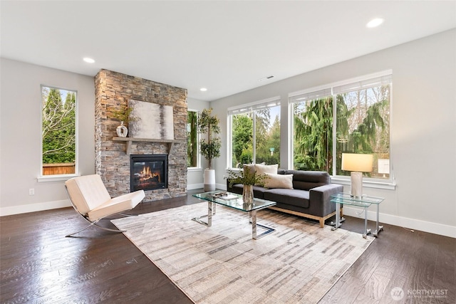 living room with a stone fireplace, wood-type flooring, recessed lighting, and baseboards