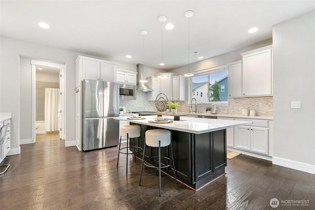 kitchen with appliances with stainless steel finishes, a center island, dark wood-type flooring, and wall chimney range hood