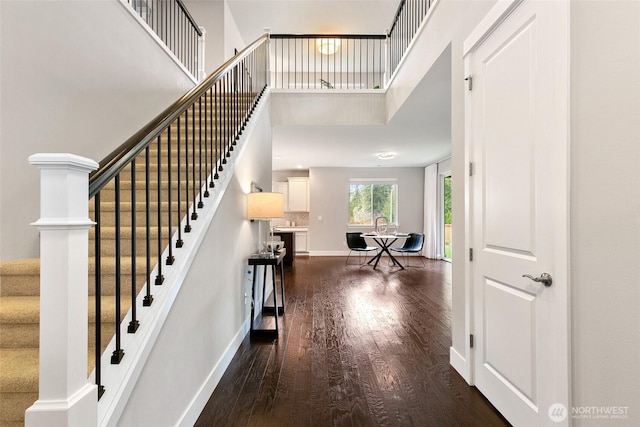 entrance foyer featuring a towering ceiling, dark wood-style floors, stairs, and baseboards