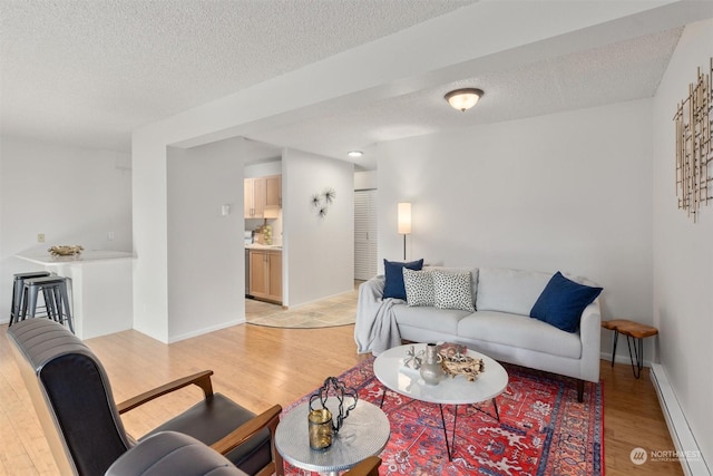 living room with baseboard heating, light hardwood / wood-style floors, and a textured ceiling