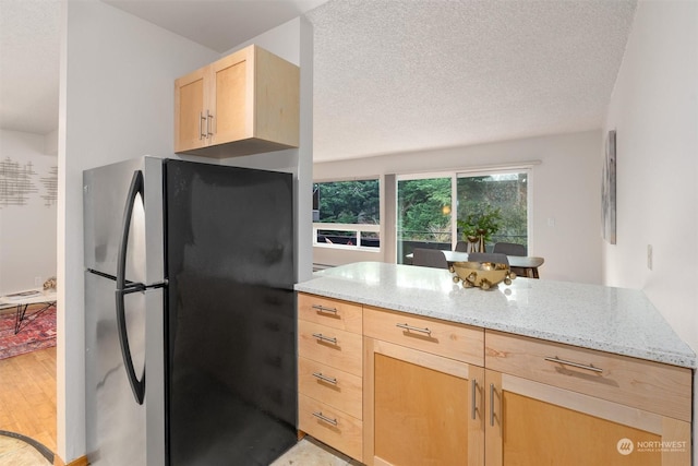 kitchen featuring stainless steel refrigerator, light stone countertops, light brown cabinets, a textured ceiling, and light hardwood / wood-style flooring