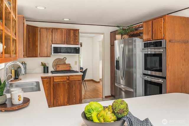 kitchen with a sink, recessed lighting, stainless steel appliances, brown cabinetry, and light countertops