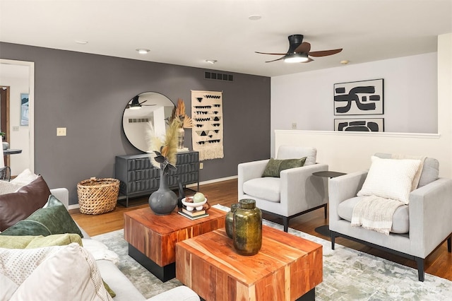 living room featuring ceiling fan, visible vents, baseboards, and wood finished floors