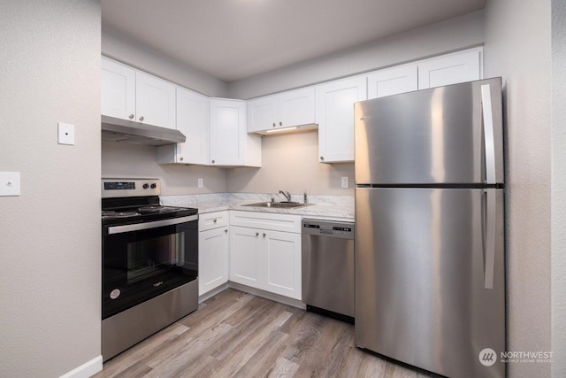 kitchen with appliances with stainless steel finishes, white cabinetry, sink, light stone countertops, and light wood-type flooring