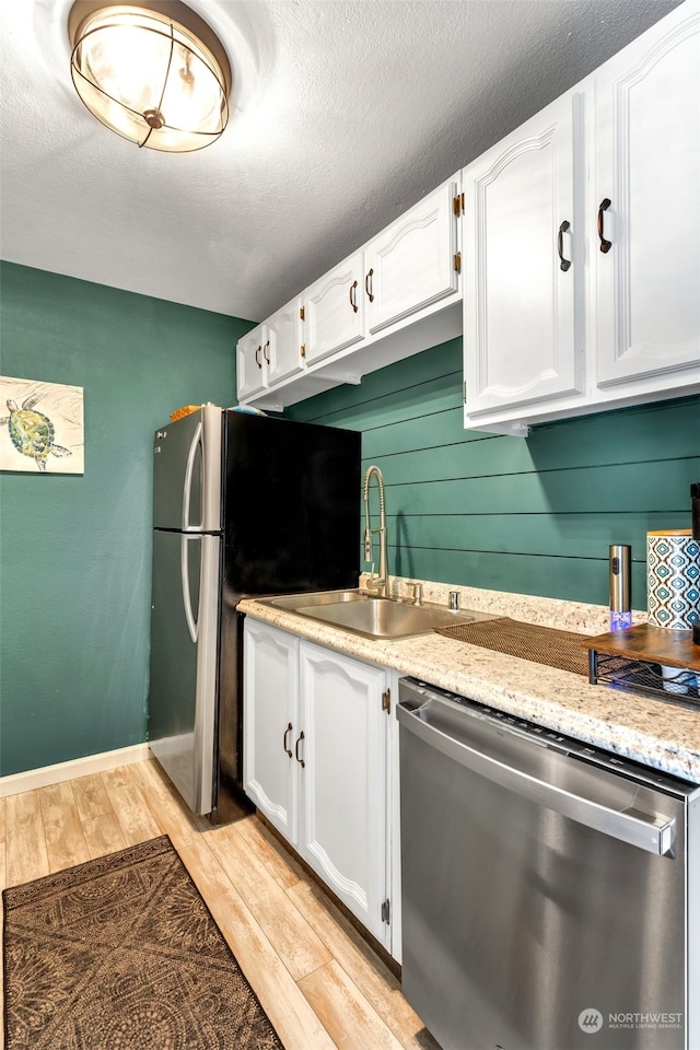 kitchen featuring appliances with stainless steel finishes, sink, white cabinets, light stone countertops, and light hardwood / wood-style flooring