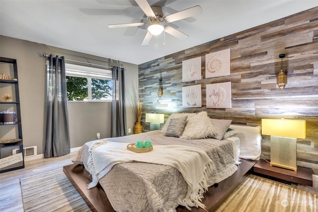 bedroom with ceiling fan, wood walls, and light wood-type flooring