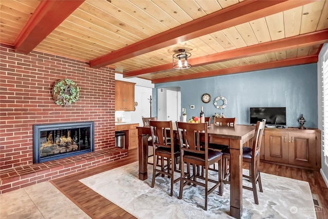 dining room featuring beamed ceiling, a brick fireplace, hardwood / wood-style floors, and wood ceiling