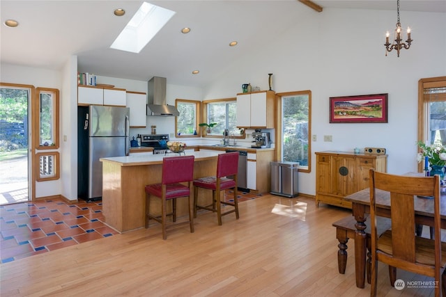 kitchen featuring wall chimney exhaust hood, decorative light fixtures, appliances with stainless steel finishes, a kitchen island, and white cabinets