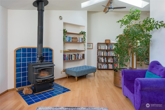 living area with hardwood / wood-style flooring, a skylight, ceiling fan, and a wood stove