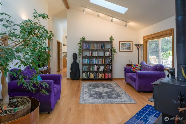 sitting room with a wood stove, rail lighting, vaulted ceiling with skylight, and light wood-type flooring
