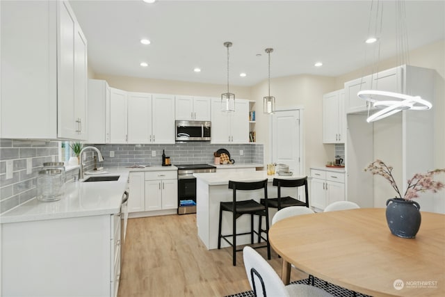 kitchen with a kitchen island, pendant lighting, white cabinetry, sink, and stainless steel appliances