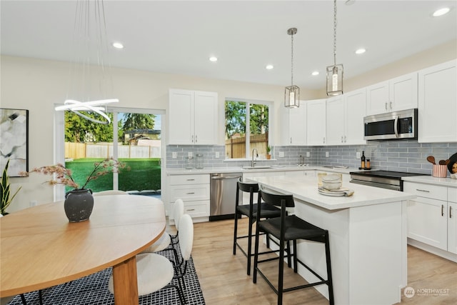 kitchen with a kitchen island, sink, white cabinets, hanging light fixtures, and stainless steel appliances