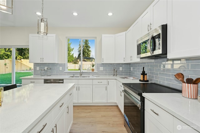 kitchen with decorative light fixtures, sink, white cabinets, stainless steel appliances, and light hardwood / wood-style flooring