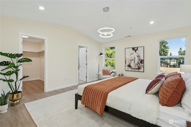 bedroom with lofted ceiling, a spacious closet, light hardwood / wood-style flooring, and a notable chandelier