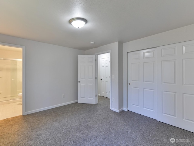 unfurnished bedroom with ensuite bath, a closet, and dark colored carpet