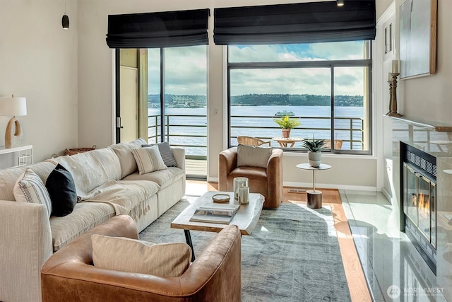 living room featuring a water view, a fireplace with flush hearth, and baseboards