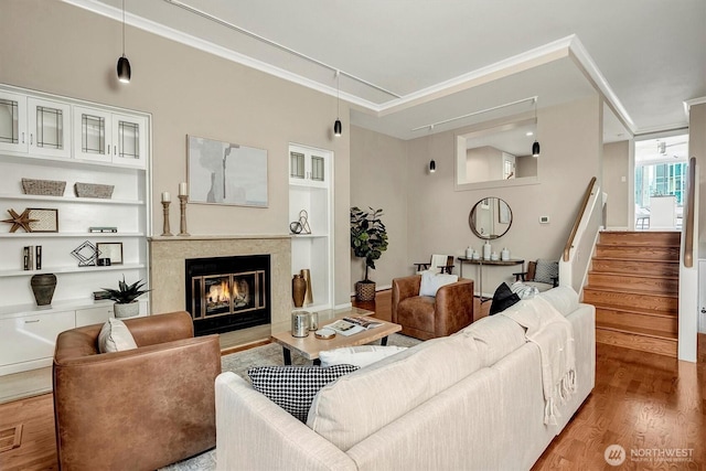 living room with a fireplace, wood finished floors, built in features, stairway, and crown molding