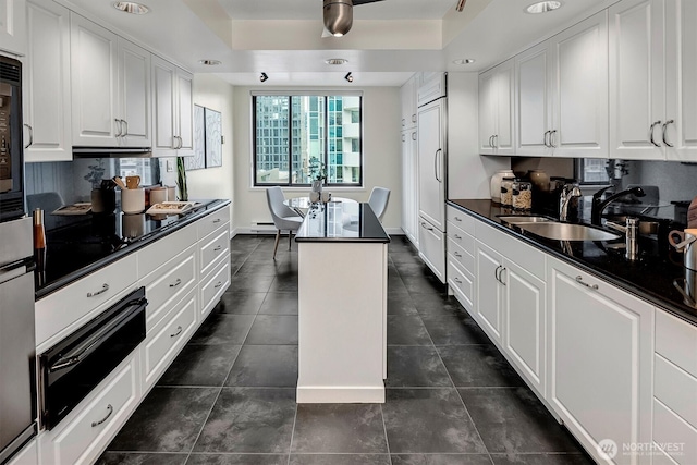 kitchen featuring a sink, white cabinetry, a warming drawer, dark countertops, and a raised ceiling