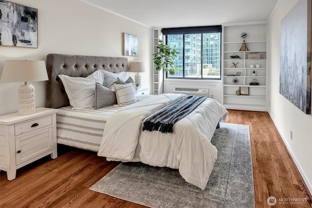 bedroom with baseboards, a wall mounted AC, wood finished floors, and crown molding