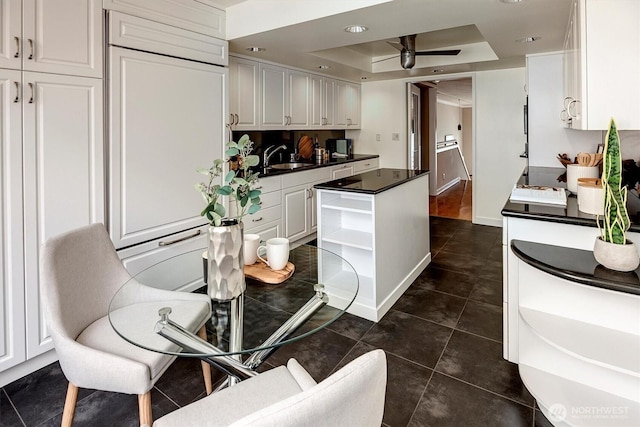 kitchen with white cabinets, a center island, open shelves, a tray ceiling, and dark countertops