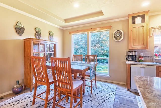 dining space with ornamental molding, a raised ceiling, and light hardwood / wood-style floors