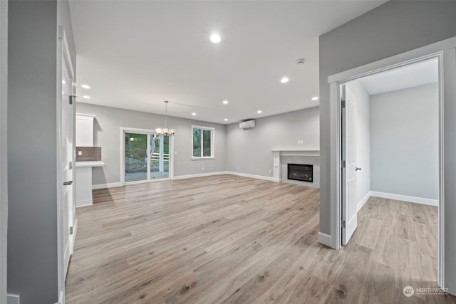 unfurnished living room featuring a wall unit AC, a notable chandelier, and light wood-type flooring