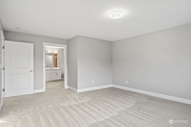 unfurnished bedroom featuring ensuite bathroom, sink, and light carpet