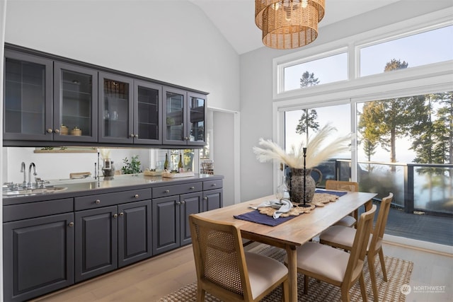 dining room with an inviting chandelier, sink, light hardwood / wood-style floors, and high vaulted ceiling