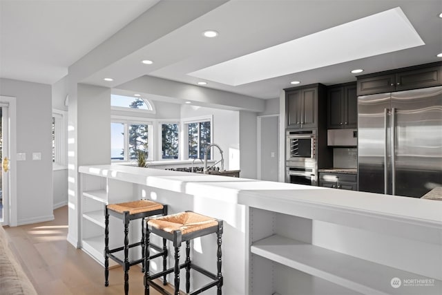 kitchen featuring a breakfast bar, a skylight, kitchen peninsula, stainless steel appliances, and light wood-type flooring